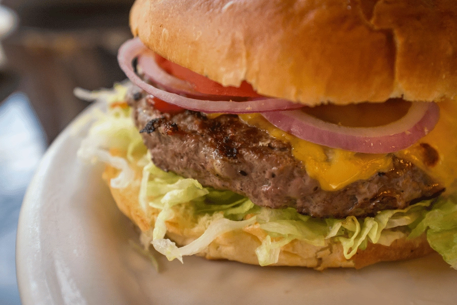 close up of cheeseburger with lettuce, tomato, and onion as toppings